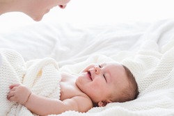 Close up of baby smiling at his mother. Newborn child looking up at mother . Love, cheerful, realtionships.
