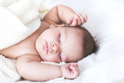 Close up portrait of sleeping sweet baby boy in a bright bedroom covered with white blanket. Love, cheerful, mother's care.
