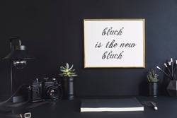 Black design room with mock up poster frame, plants in black cans, notebook and accessories. Modern and stylish black interior.