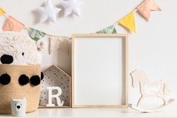 Stylish and modern scandinavian childroom interior with mock up photo or poster frame on the white shelf. Toys, teddy bear in basket, rocking horse  and hanging cotton colorful flags and stars. Blank.