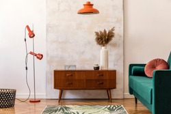Stylish compositon of retro home interior with vintage cupboard, velvet sofa, flowers in vase, design orange lamps , elegant accessories and abstract paintings. Minimalistic concept. Nice home decor. 