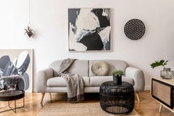 Stylish and scandinavian living room interior of modern apartment with gray sofa, pillows, plaid, plants, design wooden commode, black table, lamp, abstrac paintings on the wall.  Modern home decor.