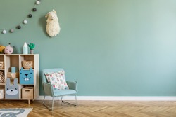 Stylish scandinavian newborn baby room with wooden cabinet, toys, children's armchair and pillow. Modern interior with eucalyptus background walls, wooden parquet and cotton balls. Cute home decor.