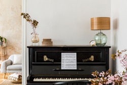 Stylish composition at living room interior with black piano, dried flowers in vase, gold clock, design lamp, boxes, copy space and elegant presonal accessories in modern home decor.