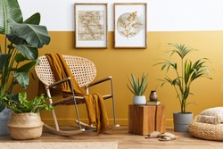 Stylish composition of living room interior with design rattan armchair, two mock up poster frames, plants, cube, palid and personal accessories in honey yellow home decor. Template.