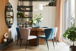 Stylish composition of elegant dining room interior design with velvet armchairs, design rouded wooden table and beautiful personal accessories. Glamour interior design inspiration. Template.