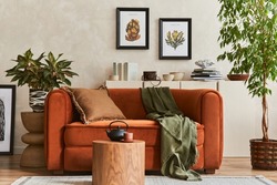 Creative composition of stylish living room interior with mock up poster frames, orange sofa, beige commode, coffee table and stylish personal accessories.Plants lover space. Template.