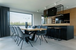 Creative composition of dining room and kitchen open space interior design. Rectangle family table, velvet chairs, wooden ergonomic biuld-in kitchen and elegant personal accessories. Template.