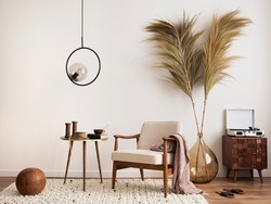 Interior design of aesthetic and minimalist living room with boucle armchair, wooden coffee table, pedant lamp, beautiful leafs in vase, decoration and personal accessories. Copy space. Home decor.