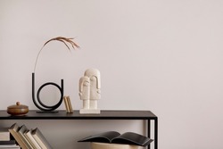 The stylish composition of minimalistic interior with copy space.  Black commode, vase with dried flowers, sculpture and personal accessories. Beige wall. Home decor. Template. 