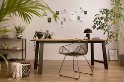 Aesthetic interior of home office interior with design chair, wooden desk, plants, shelf, office accessories, post cards, photos and decoration. Minimalist home decor. Template.	

