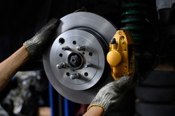 Car mechanic installing two piston brake calipers and disc brake rotor.