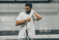 Beautiful man playing paddle tennis, racket in hand wipes the sweat. Young sporty boy at the end of the match. Sweaty padel athlete ready to take shower. Sport, health, youth and leisure concept