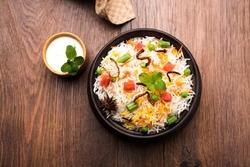 Indian Vegetable Pulav or Biryani made using Basmati Rice, served in a wooden bowl with yogurt. selective focus

