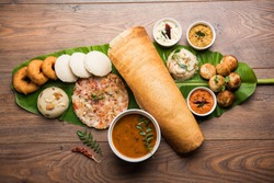 Group of South Indian food like Masala Dosa, Uttapam, Idli/idly, Wada/vada, sambar, appam, semolina halwa, upma served over banana leaf with colourful chutneys, selective focus