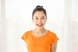 The half length shot of a beautiful face Asian woman with a black hair bun, smiling at the camera happily. A simple female portrait shot with natural light. Showing positive and friendly gestures.