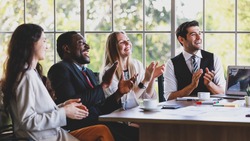 Group of four professional multiracial businessmen and businesswomen sitting and clapping hands to celebrate the new project ideas in partners company meeting at the modern office working table