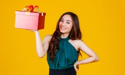 Happy smile face cute Asian girl with dark hair holding gift box with delightful and excited, studio shot on yellow background. Celebrate and festival concept