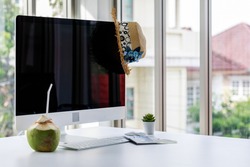 Black blank computer monitor screen for summer travel booking advertisement ads and copy space with wide brim hat coconut water with straw keyboard mouse tree pot in front blurred garden background.