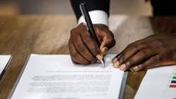Close up and selective focus on African black formal professional business male hands holding pen, signing in white paper form or application to confirm and deal contract agreement on table