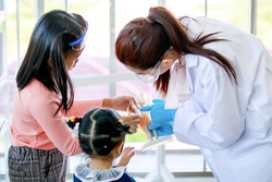Asian female scientist teacher wears safety goggles white lab coat rubber gloves teaching little curious preschool girls observing studying on human anatomy from hand skeleton model in laboratory.