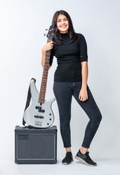 Portrait shot of attractive young Thai-Turkish teenager standing and holding the bass guitar on the amplifier. Mixed-race junior bass guitarist looking at the camera isolated in white background