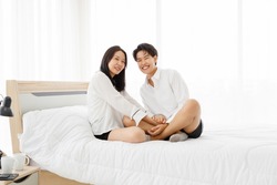 LGBTQ couple lovers, a handsome girl as man or butch and femme, spending and sharing loving time in white bedroom with fun, warmth, and happiness.