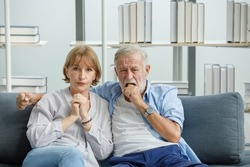 Caucasian old senior grandparents couple in casual wear gray bearded and hair grandpa husband and grandma wife sitting stress horror thrilling worrying watching scary movie together at home.