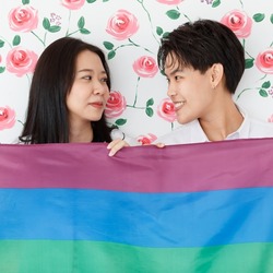 LGBTQ couple lovers, a handsome girl as a man or butch femme holding the rainbow flag the symbol of LGBT, spending and sharing loving time with fun, warmth, and happiness.