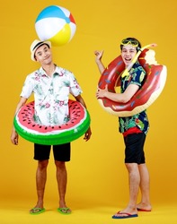 Two young Asian boys in summer costume laugh as enjoy playing fun outdoor game with ball float, donut tube, and snorkel at swimming pool party as family recreation to relax on vacation of hot season.