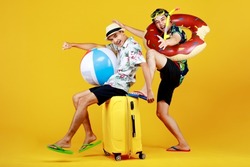 Naughty Asian boy enjoys sitting on luggage and exciting to travel to beach and sea to play fun water sport with float ball together with friend in swimming tube and snorkel for outdoor scuba diving.