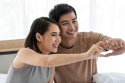 Portrait of cute smiling young Asian lover couple in casual clothes showing gesture in heart sign together. Selective focus at the face with blurred heart, selective focus on faces