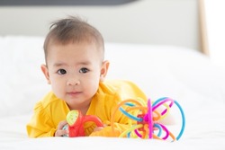 Portrait innocent baby child holding and playing toy on white bed in bedroom with bright soft light in morning in background.