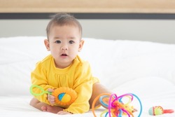 Portrait innocent baby child holding and playing toy on white bed in bedroom with bright soft light in morning in background.