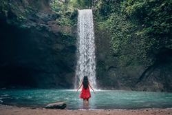 Girl in red dress at amazing Tibumana Waterfall Bali - the best cascade in Indonesia