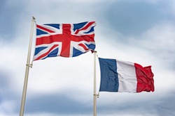 Flag of the United Kingdom and the flag of the Republic of France fluttering in the wind against a blue sky. The concept of friendship or cooperation of Great Britain and France.
