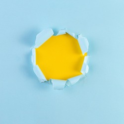 Ripped Paper Hole with yellow coloured background. Torn hole in blue paper, ripped edges. Copy space for your design.