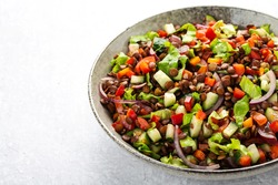 salad with lentils and vegetables in a deep plate on a gray background, vegetarian food