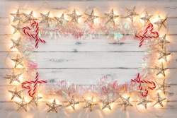 A string of golden star christmas lights, tinsel and candy sticks, on a destressed woodern background, creating a border around an empty space for copy