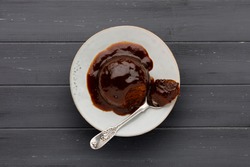 Sticky toffee sponge cake, with a sticky toffee sauce, on a white plate with a spoon, on a dark grey wooden surface with space for copy