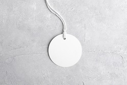 Round white tag mockup with white cord, close up. Blank paper price tag isolated on grey stone background with copy space.