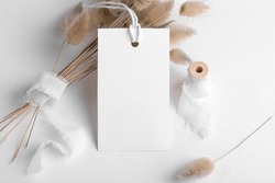Rectangle white tag mockup on a white background with cotton string and boho decoration, dry plants, element for packing. Label product bohemian mockup copy space for text and natural eco design