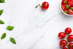 Red cherry tomatoes bunch and green basilic leaves on a white marble background, salad in a white bowl. Copy space in the middle to insert text or design, top shot