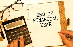 Finance and economics concept. The man is holding a pen and a notebook with the inscription - END OF FINANCIAL YEAR. In the background are financial charts, charts and a calculator.