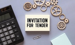 Text INVITATION FOR TENDER on a white card with a yellow notepad next to hand-to-pen, business concept