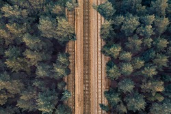 Rail rails on sleepers in the middle of a green forest in the evening in clear weather. Background on the theme of rail travel by train. Aerial overhead drone shot.