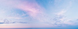 Calm, quiet, gentle clouds - a wide panoramic view of the sky before sunset. Pink clouds in blue clear skies on a summer evening. Panorama of the blue-pink sunset sky - the gentle sky on the horizon