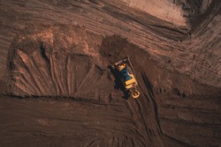 Yellow tracked bulldozer performs earthworks - aerial view shot. Yellow tracked tractor rakes the ground to build an asphalt road. Earthen bulldozer works during the construction of the route road.