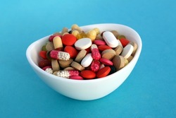 A small white plate contains many pills and capsules of different colors.