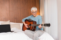 Lovely mature woman playing guitar in her bedroom, Free time and hobbies concept